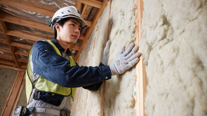 男性がヘルメットで断熱材を壁に施工する作業