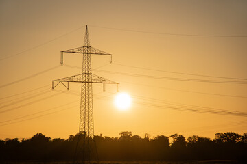 Transmission tower or high-voltage electricity pylon at bright sunset or sunrise, landscape format, symbol of energy and power generation in Germany.