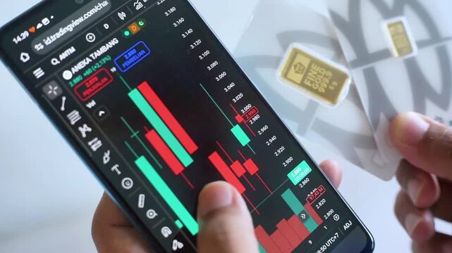 Balikpapan, 6 Spetember 2025. Close-up of hand holding 5g and 1g Antam pure gold and smartphone with stock market chart. Gold investment and stock trading concept.