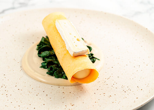 French omelette with Brie cheese and spinach, close-up restaurant style. Close-up of a French omelette filled with spinach and soft Brie cheese, styled on a ceramic plate in a fine dining presentation