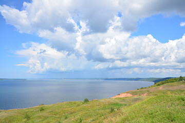 Scenic view of a large lake with a cloudscape, with a grassy hill in the foreground