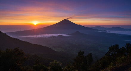 Fototapeta premium Sunrise paints a vibrant sky over a majestic volcano, its peak smoking gently, as layers of mountains stretch into the distance.