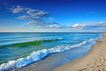 Obraz premium Tranquil beach scene at dawn or dusk. Ocean waves gently lap the shore. Light blue sky with puffy clouds