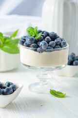 Panna cotta with fresh blueberries in a clear bowl.