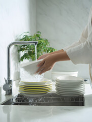 Person Washing White Plates in Sink with Running Water