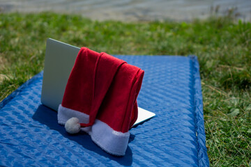 A santa hat on a laptop on a blue blanket near a lake, concept of remote work, summer holidays, christmas promotions