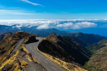Scenic mountain road at Miradouro do Lombo do Mouro, Madeira, winding through dramatic peaks with clouds and the Atlantic Ocean in the distance.