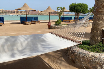 A white hammock swing between two palm trees. The hammock looks cozy. Detail. Empty hammock swinging in nature