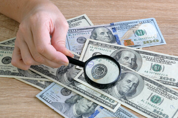 hand with magnifying glass checking 100 USA dollar banknote on money background, exchange money