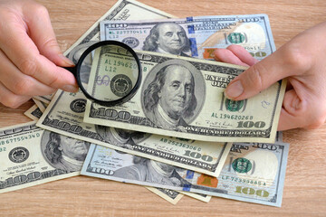 hand with magnifying glass checking 100 USA dollar banknote on money background, exchange money