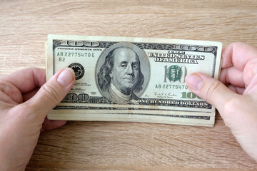 hand with magnifying glass checking 100 USA dollar banknote on money background, exchange money