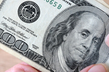 hand with magnifying glass checking 100 USA dollar banknote on money background, exchange money