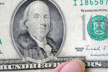 hand with magnifying glass checking 100 USA dollar banknote on money background, exchange money