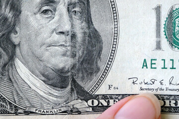 hand with magnifying glass checking 100 USA dollar banknote on money background, exchange money