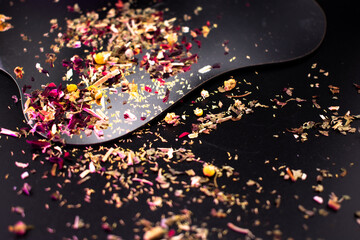 Colorful dried herbal tea blend with rose petals, chamomile, and spices scattered on a black surface, symbolizing wellness, natural health, and aromatic flavor.