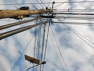 A chaotic yet fascinating view of an urban power pole, with a complex network of tangled wires and cables against a cloudy sky, representing modern city infrastructure.