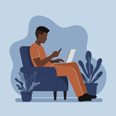 A young man simultaneously uses a laptop and smartphone in a comfortable armchair at home, representing remote work, online learning, or digital connectivity.