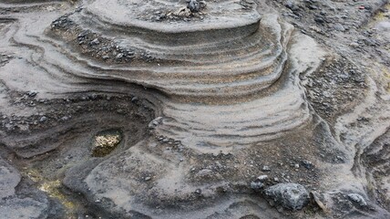 Close up of undulating layers in dark volcanic rock stone layers with subtle golden streaks, sand...