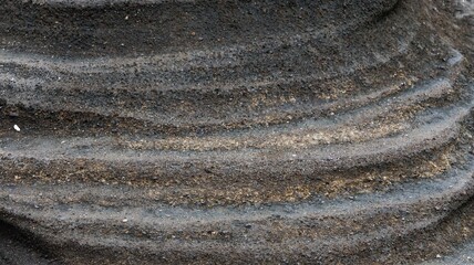 Close up of undulating layers in dark volcanic rock stone layers with subtle golden streaks, sand...