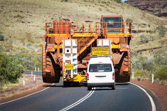 Massive mining truck escorted by pilot vehicle on a remote highway.
