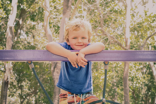 Relaxed little boy smiling at top of spiderweb climbing net at the playground