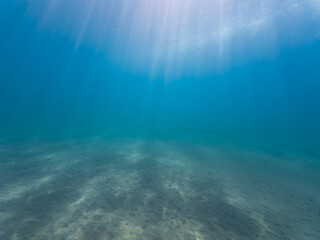 Peaceful underwater background with beautiful sunbeams shining through the clear blue ocean water to the serene sandy sea floor.