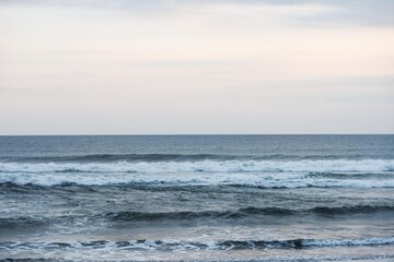 Tranquil ocean waves rolling toward the shore under a soft gradient sky transitioning from blue to pastel pink at dusk with a clear contrast line between sea and sky