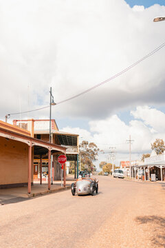 Fototapeta Vintage car driving towards stop sign in small country town