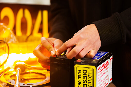 Male mechanic hand working on wiring testing light with battery in workshop