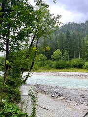 Impressive rocky mountain cliff and green forest by a clear alpine river in Nationalpark Gesäuse, Austria. Dramatic landscape scenery with rugged rocks, turquoise water and nature. Ideal for travel.