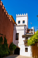 Historic whitewashed building with tower and balcony in narrow street of Seville, Spain, under bright blue summer sky