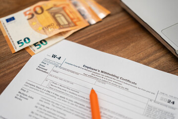 Obraz premium Euro bills lie scattered near essential W-4 form on table alongside pen and laptop as worker prepares to fill out form to ensure correct federal tax deductions