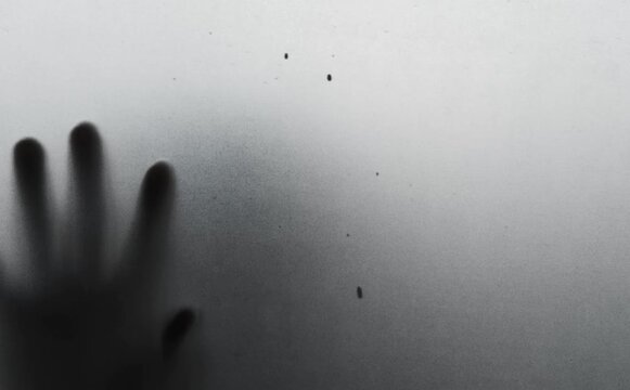 Shadow of scary horror man behind the matte cloudy white glass in soft focus. Blurry hand and body figure abstraction.