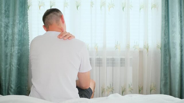 Young man with neck pain, accident or injury for bad posture in bedroom at home. Tired, illness male person with spine muscle sprain for fatigue at house.