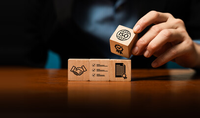 Hand stacking wooden blocks with quality, certification, and ISO icons, symbolizing business standards, process management, quality assurance, compliance, trusted partnership for sustainable growth.