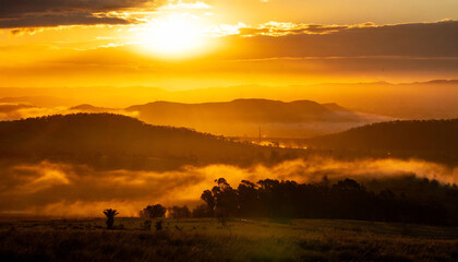 Golden sunrise over mountain landscape, sunlight rays streaming through morning mist, serene valley