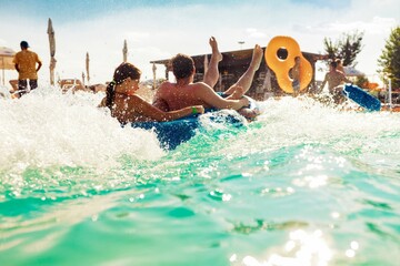 A couple is propelled forward on a bright blue raft through the frothy waves of the wave pool