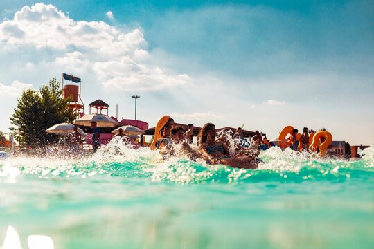 A group of friends laughs and splashes, riding the waves at a waterpark wave pool on a sunny afternoon. Water splashes everywhere as they enjoy a refreshing summer day in Orlando - Powered by Adobe