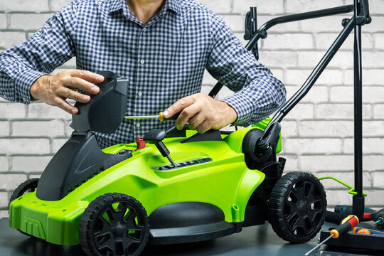 Technician, man in uniform is repairing a electric cordless lawn mower on workbench. Small business.