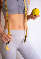 Woman in sportswear holding measuring tape and apple, symbol of weight loss and balance. 