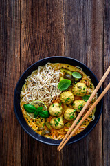Curry soup with meatballs and zucchini with Asian noodles on wooden background	