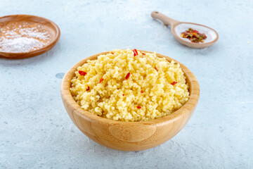 Cooked millet in a wooden bowl on a blue background, with salt and pepper. Healthy vegan side dish