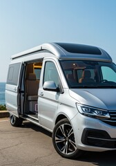 Silver camper van with open door overlooking coastal scenery