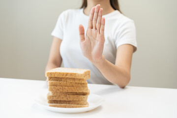 Gluten allergy, asian young woman hand push out, refusing to eat white bread slice on plate in breakfast food meal at home, girl having a stomach ache. Gluten intolerant and Gluten free diet concept.