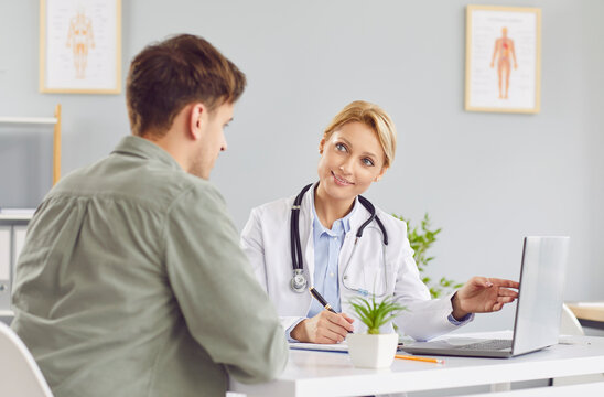 Young female professional doctor physician consulting young male patient, talking to man client at regular medical visit, online appointment, laptop screen show for diseases treatment, adult checkup