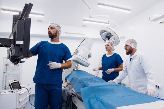 Medical team in blue scrubs collaborating in a modern operating room, preparing for an angiograph procedure with advanced imaging equipment and sterile environment for patient care