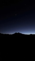 Fototapeta premium Serene Night Sky with Silhouette of Mountain Range Against Subtle Starry Backdrop and Hints of Twilight Horizon