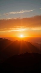 Obraz premium Majestic sunset view over mountain range with vibrant sky hues, glowing sun descending behind the peaks, creating dramatic silhouettes and warm atmospheric colors