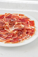 Thin Slices of Jamon Iberico Arranged on White Round Plate for Serving