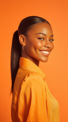 Smiling young woman with sleek ponytail wearing orange shirt and gold hoop earrings posing against vibrant orange background with confident and joyful expression